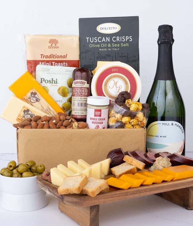 A charcuterie gift set with Tuscan crisps, focaccia crackers, 3 cheeses, olives, mustard, suasage almonds, chocolate-covered popcorn and a bottle of California Sparkling Wine.