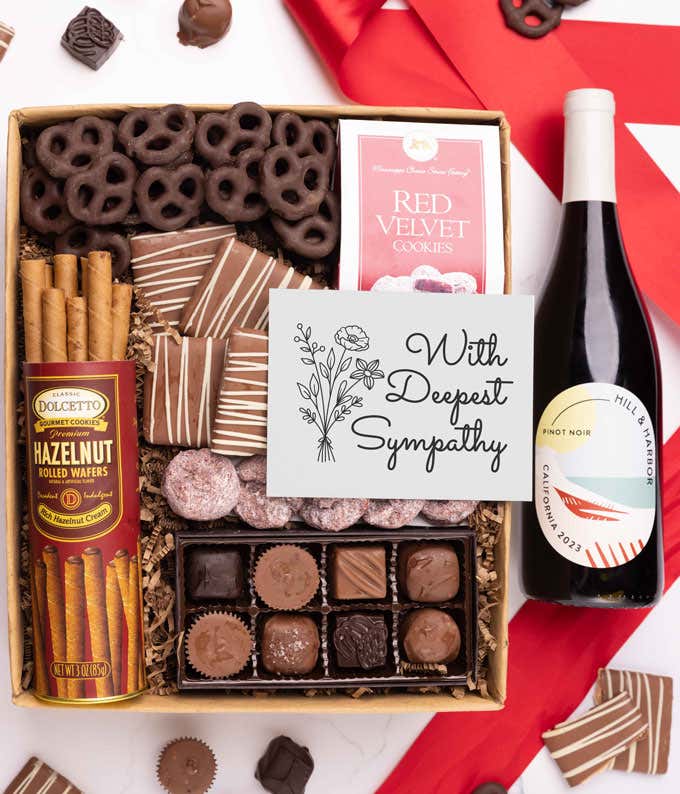 A gift box with chocolate pretzels, chocolate graham crackers, red velvet cookies, hazelnut wafer rolls, an 8 piece box of chocolates, a bottle of red wine and a Sympathy message card.