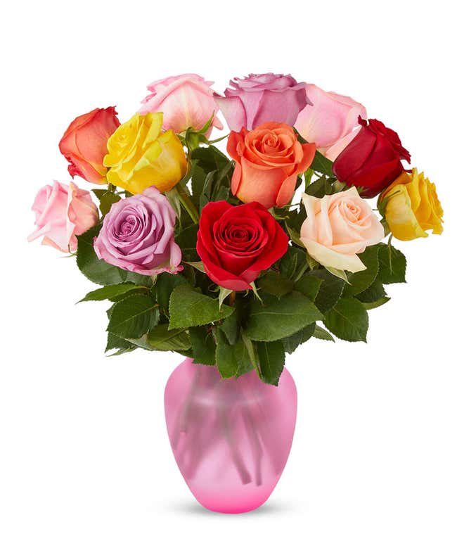 A bouquet of multicolored roses in a clear vase, featuring red, pink, orange, yellow, peach, and lavender blooms, arranged with green leaves for a vibrant and cheerful display.