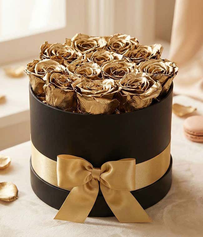 One dozen gold preserved roses arranged in a black hat box with a gold ribbon.