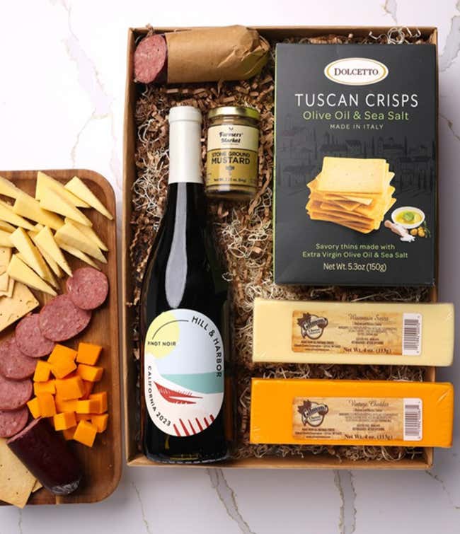 A gift box with a bottle of California Pinot Noir, two types of cheese, crackers, stone-ground mustard, and a summer sausage.