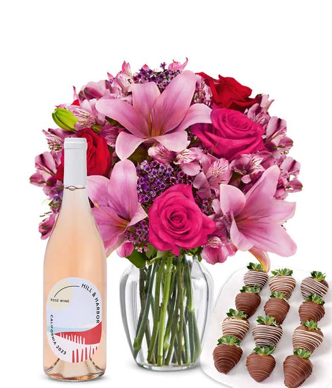 A mixed bouquet of pink and purple flowers in a clear glass vase is displayed with a bottle Hill &amp; Harbor Ros&eacute; and 12 chocolate-covered strawberries.