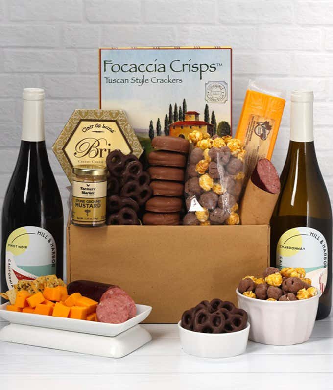 A gift set featuring two bottles of Hill & Harbor wine - white and red, focaccia crisps, 2 cheeses, mustard, summer sausage, caramel popcorn, chocolate pretzels, and 6 chocolate-covered Oreos for a sweet and savory gourmet experience.