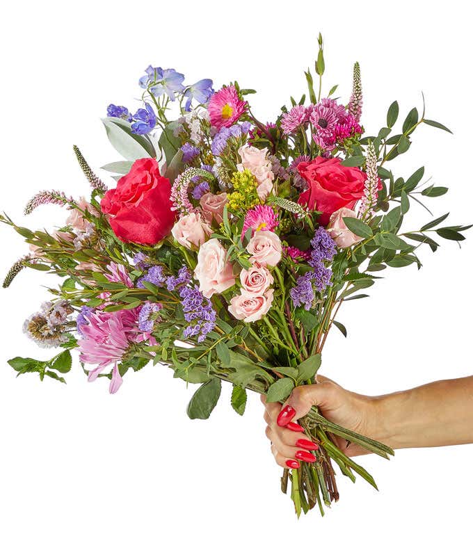 a bright bouquet of peach mini roses, hot pink full sized roses, light pink and bright pink matsumoto asters, greenery, and dark blue delphinium flowers arranged as a bouquet.