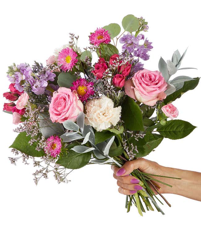 A hand-tied bouquet of pink roses, peach carnations, spray roses, succulents, and fresh greenery in a soft and graceful design.