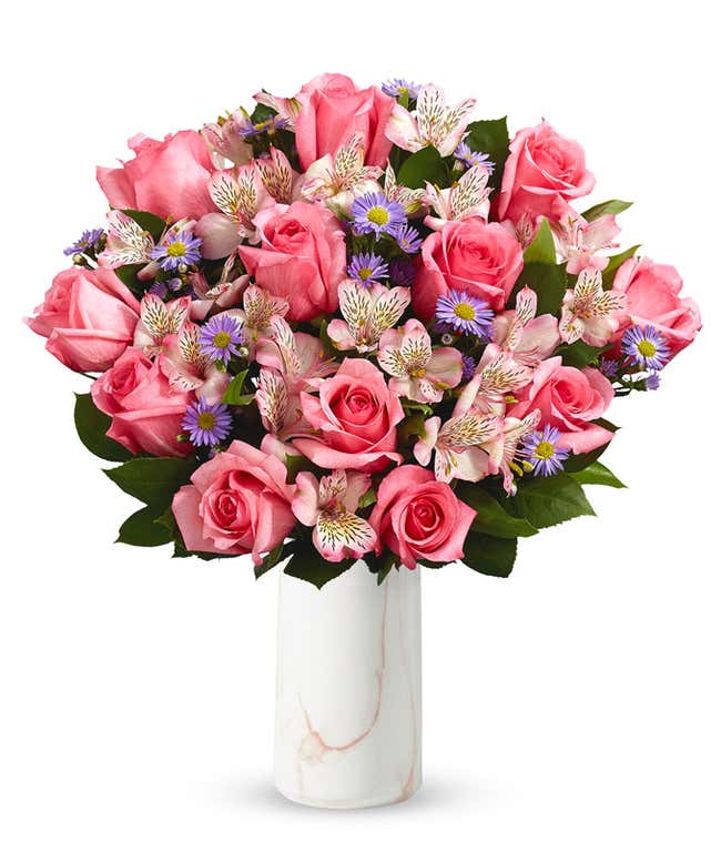 A bouquet of pink roses, white alstroemeria, and lavender aster in a glass vase 