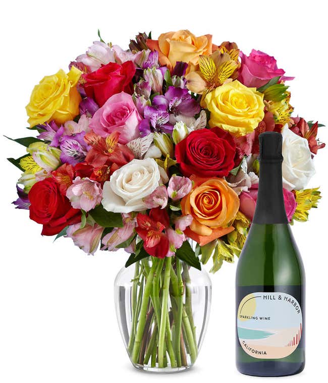 A mix bouquet of roses and alstroemeria fills a clear glass vase and is paired with a bottle of Hill &amp; Harbor California Pinot Noir.
