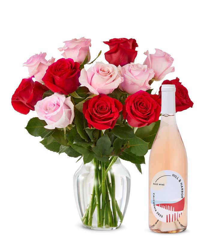 A mix bouquet of one dozen red and blush roses fills a clear glass vase and is paired with a bottle of Hill & Harbor California Rosé.