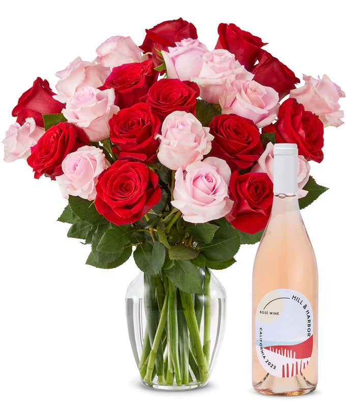A mix bouquet of two dozen red and blush roses fills a clear glass vase and is paired with a bottle of Hill & Harbor California Rosé.