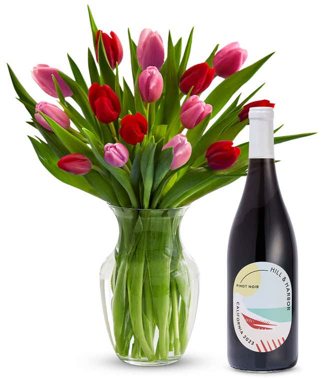 A clear glass vase filled with 15 stems of mixed red and pink tulips and bright green stems sits beside a bottle of Hill &amp; Harbor California Pinot Noir.