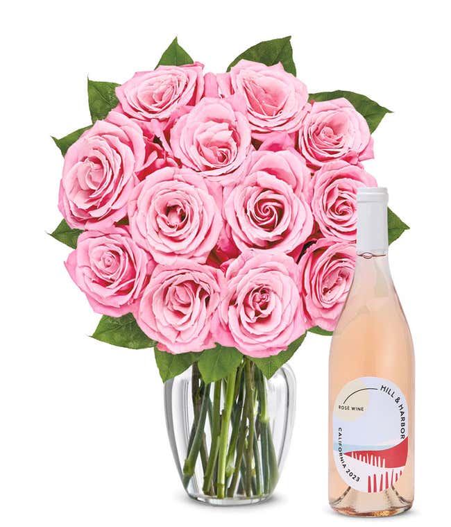 A bouquet of 12 soft pink roses arranged in a clear glass vase is displayed next to a bottle of Hill &amp; Harbor California Ros&eacute;.