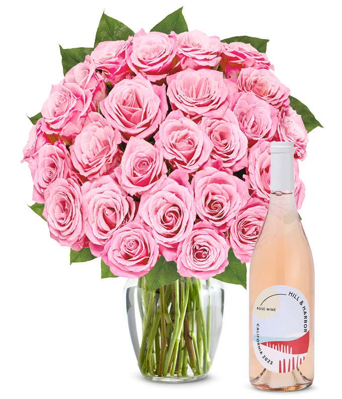 A bouquet of 24 soft pink roses arranged in a clear glass vase is displayed next to a bottle of Hill & Harbor California Rosé.