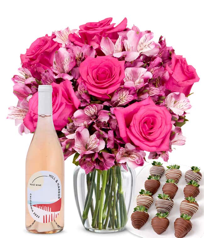 A clear glass vase filled with a pink roses &amp; alstroemeria paired with a bottle of ros&eacute; wine and 12 chocolate-covered strawberries.