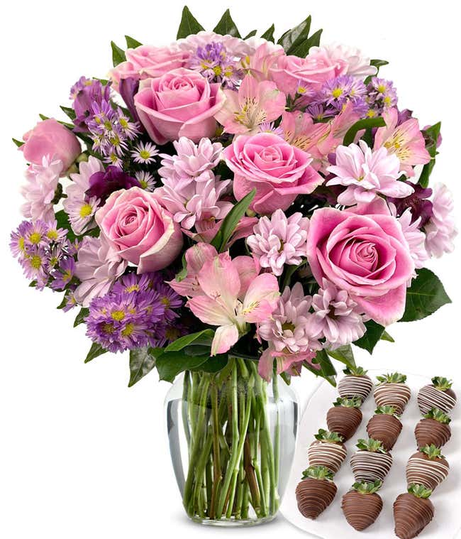  Deluxe bouquet of pink roses, lavender cushion poms, pink and purple alstroemeria, and purple asters in a clear glass vase, paired with swizzled chocolate-covered strawberries.