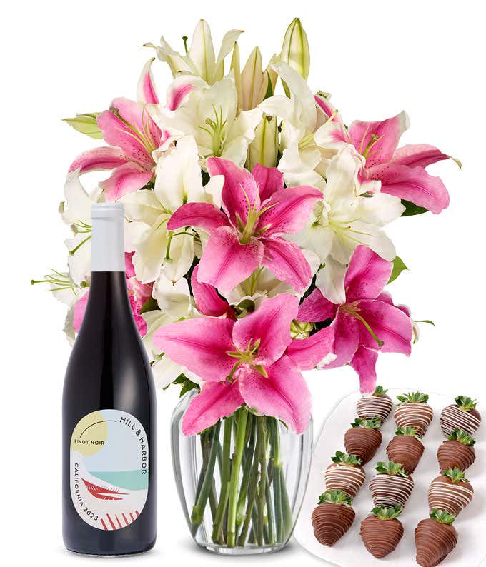 A bouquet of pink and white lilies arranged in a clear glass vase is paired with a bottle of Hill & Harbor Pinot Noir and 12 chocolate-covered strawberries.