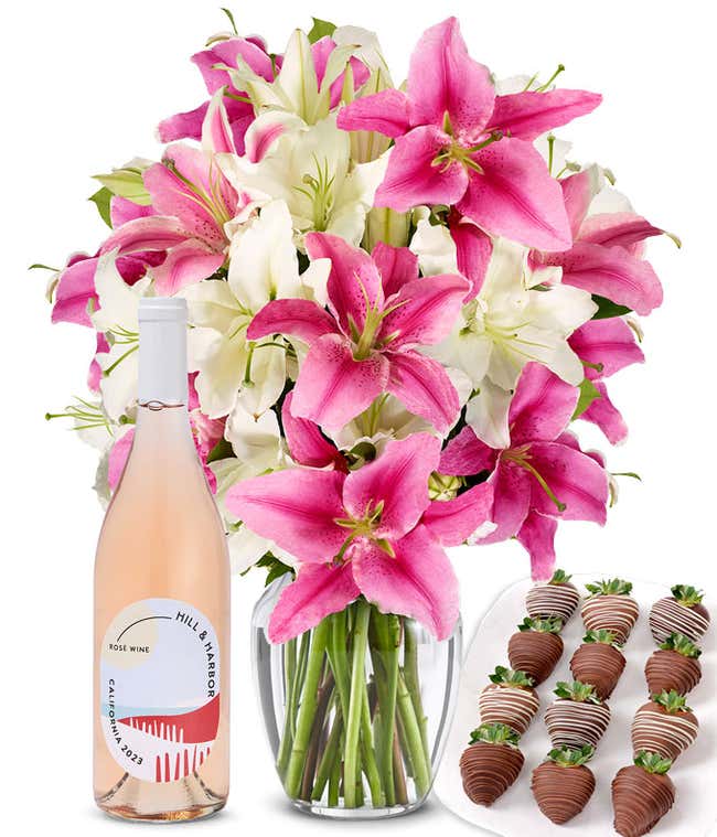 A bouquet of pink and white lilies arranged in a clear glass vase is paired with a bottle of Hill &amp; Harbor Ros&eacute; and 12 chocolate-covered strawberries.