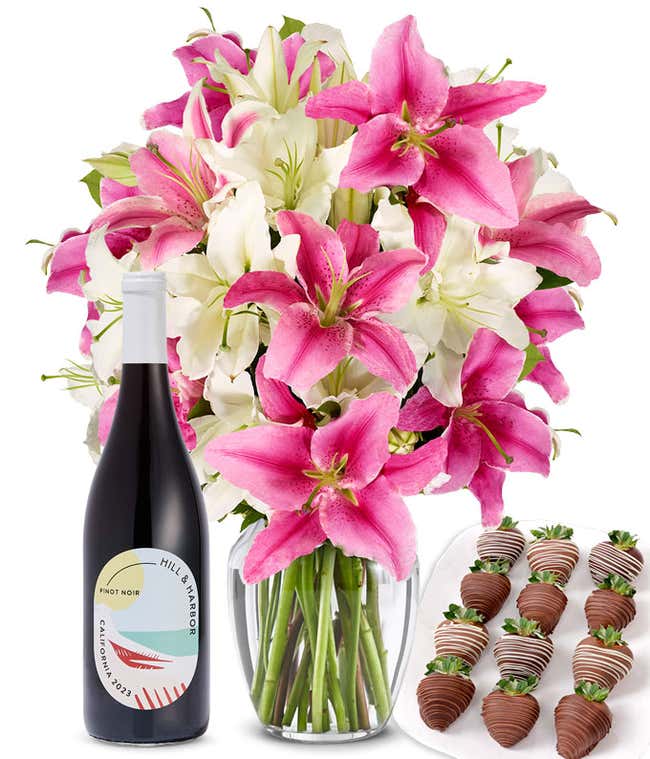 A bouquet of pink and white lilies arranged in a clear glass vase is paired with a bottle of Hill &amp; Harbor Pinot Noir and 12 chocolate-covered strawberries.