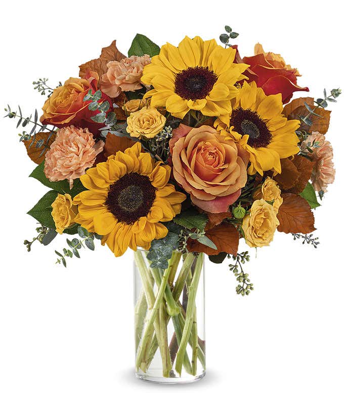 Orange and yellow roses, peach carnations, yellow sunflowers, brown copper beech, seeded & spiral eucalyptus, in a tall glass vase