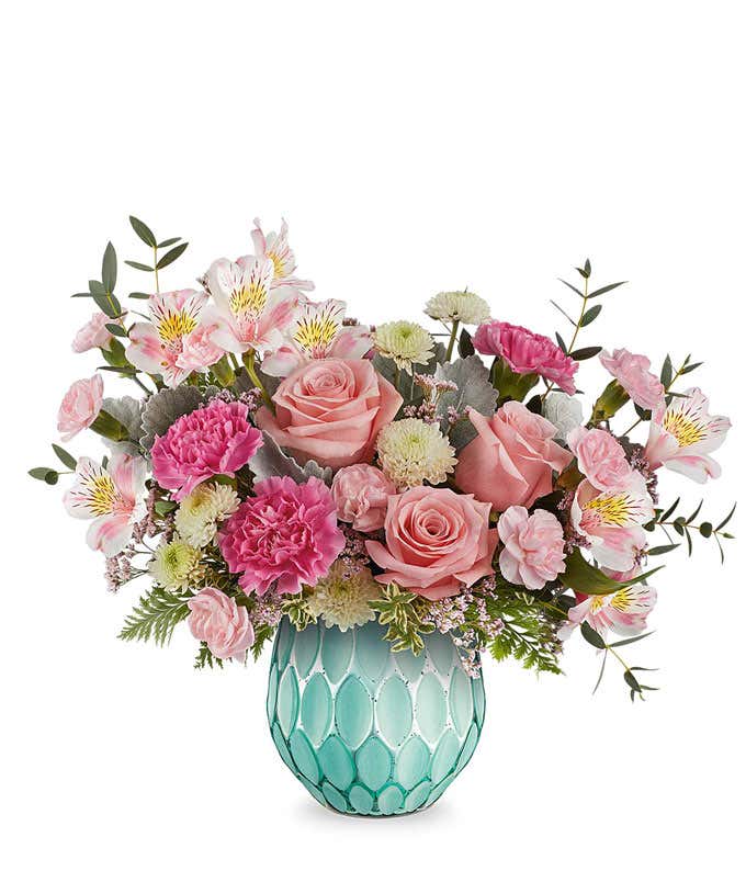 Pink roses, hot pink carnations, miniature pink carnations, white alstroemeria with pink markings, green button spray chrysanthemums, waxflower, and assorted greenery arranged in a textured turquoise glass vase.