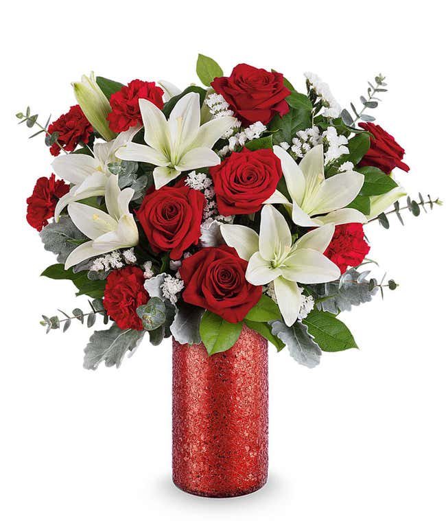 Valentine&rsquo;s Day arrangement featuring red roses, white lilies, red carnations, silver dusty miller, and lush greenery in a tall red glitter cylinder vase.