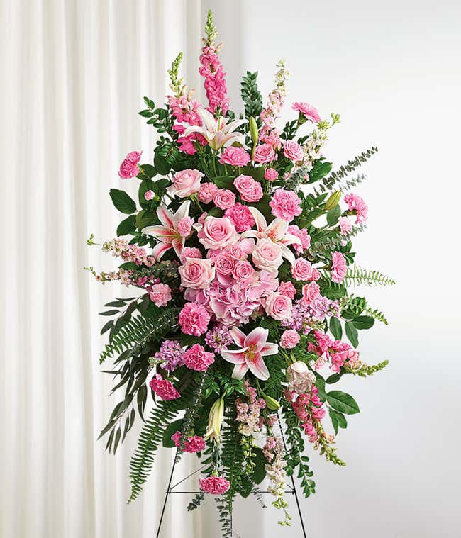 Standing spray with pink roses, lilies, carnations, and green ferns on a metal easel.