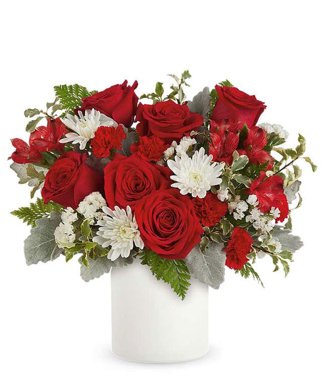 Red roses accented with white cushion mums, red spray flowers, and lush greenery arranged in a sleek white savannah vase