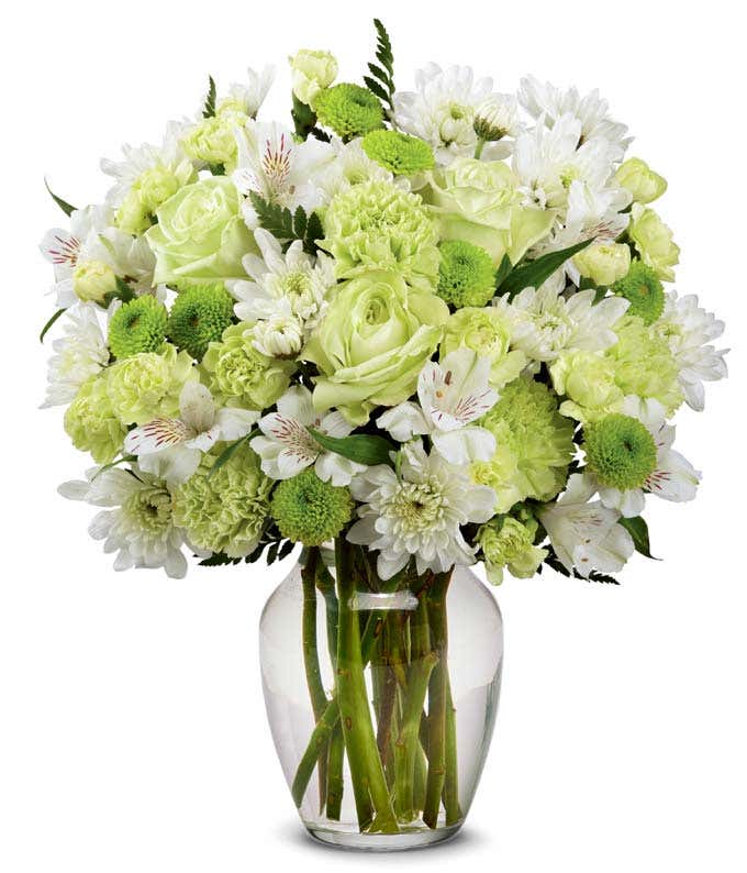 Green roses, green carnations, green button poms, and white cushion poms arranged in a clear glass vase, creating a fresh and elegant green and white floral bouquet.