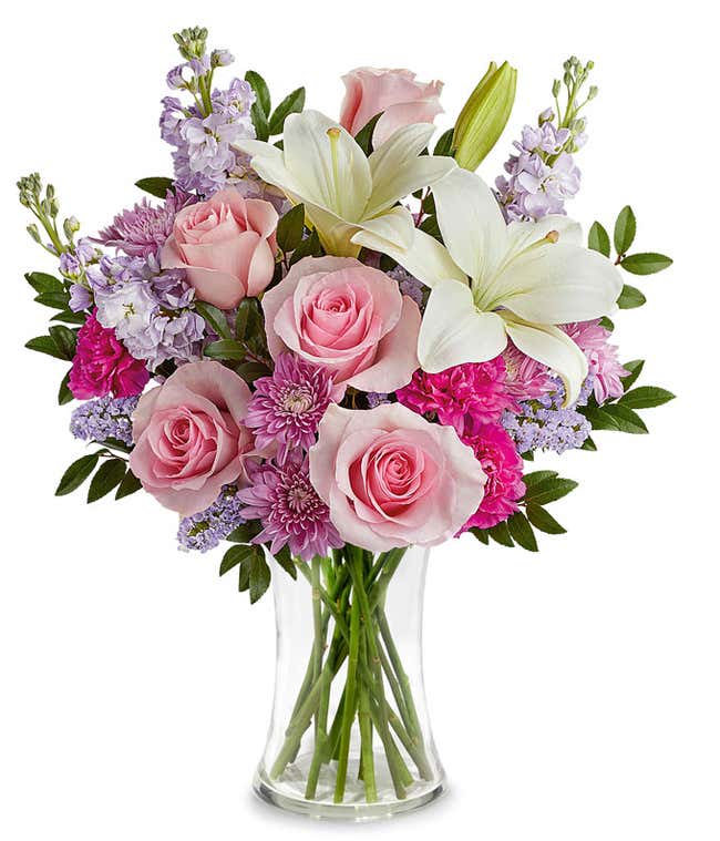 Arrangement featuring Pink Roses, White Asiatic Lilies, Hot Pink Carnations, Lavender Stock, Lavender Cushion Spray Chrysanthemums, floral greenery, all beautifully presented in a metallic lavender vase.