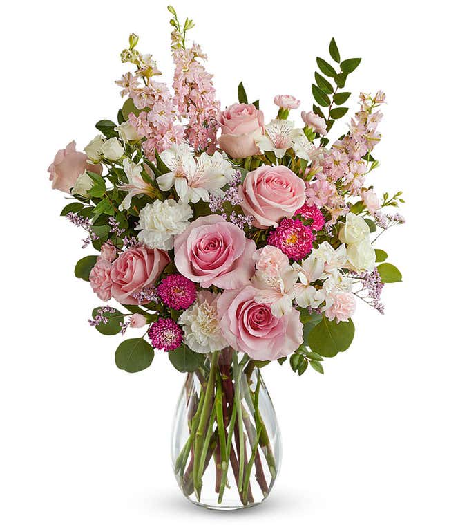 arrangement featuring Pink Roses, White Spray Roses, White Carnations, Ivory Alstroemeria, Miniature Pink Carnations, Pink Larkspur, Hot Pink Matsumoto Asters, and floral greens, all beautifully presented in a clear glass vase