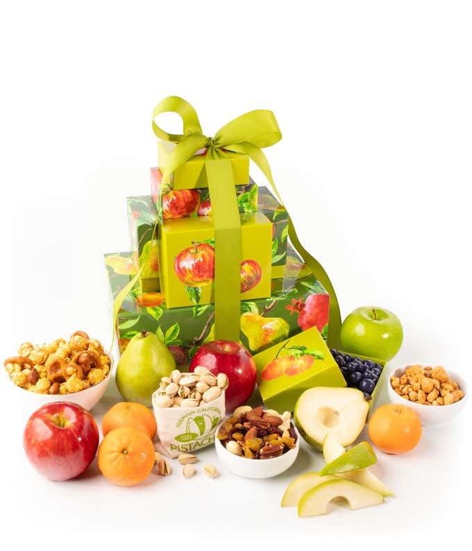 A gift tower with multiple green boxes containing fresh fruits, nuts, and chocolates, tied with a red ribbon.