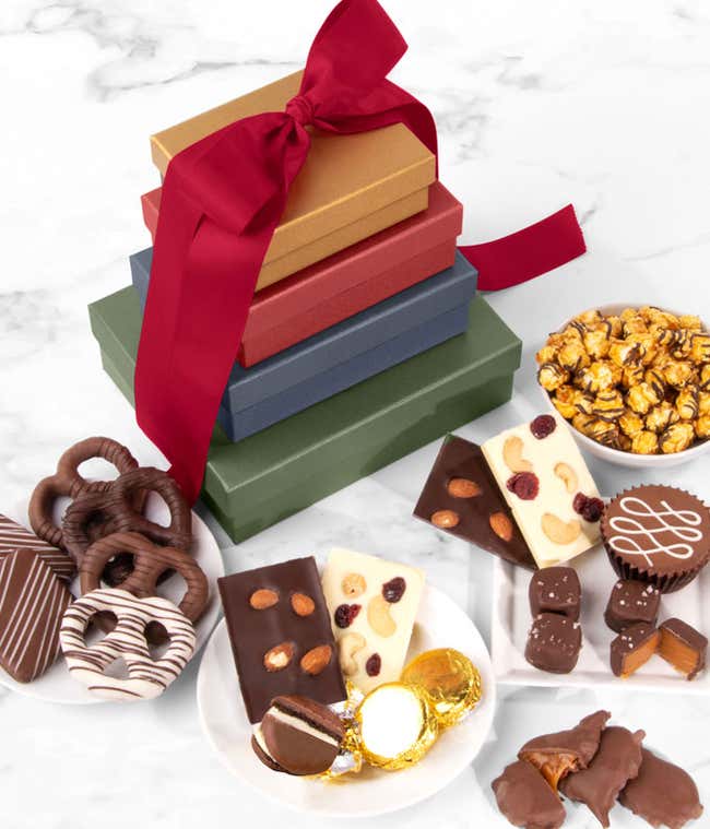 Gift tower with red ribbon filled with chocolate-covered pretzels, popcorn, nutty barks, pecan patties, graham crackers, peanut butter cup, sea salt caramels, and gold-wrapped sandwich cookies.