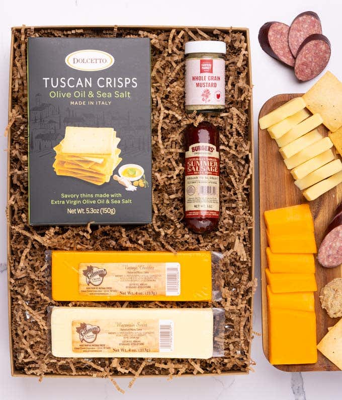 A charcuterie box with two types of cheese, crackers, stone-ground mustard, and a summer sausage.