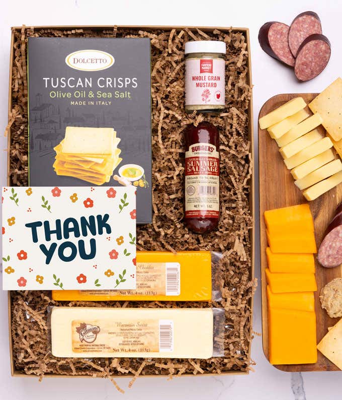 A charcuterie box with two types of cheese, crackers, stone-ground mustard, a summer sausage and a Thank You message card.