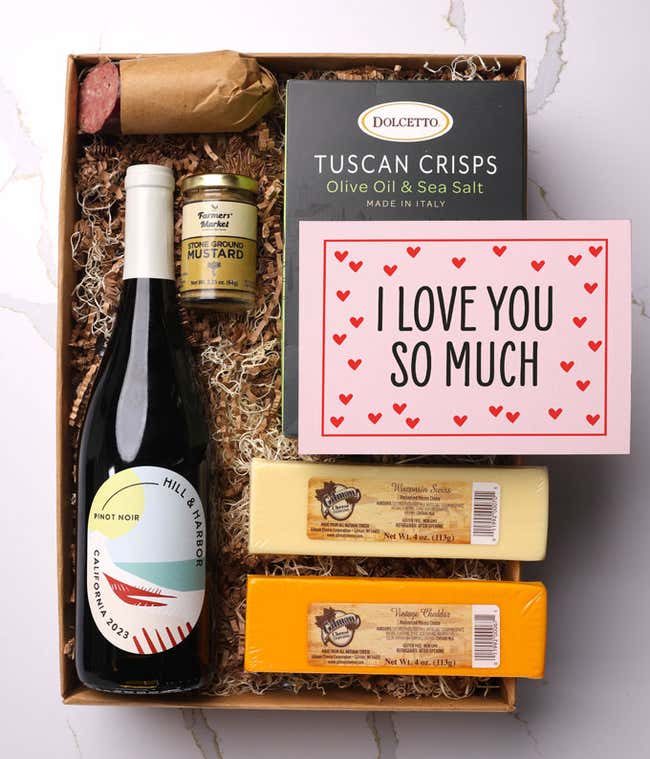 A beautifully arranged gift box featuring a bottle of Hill &amp; Harbor Pinot Noir, two hard cheeses, a jar of stone-ground mustard, gourmet crackers, savory summer sausage, and a pink card with hearts that reads 'I Love You So Much'