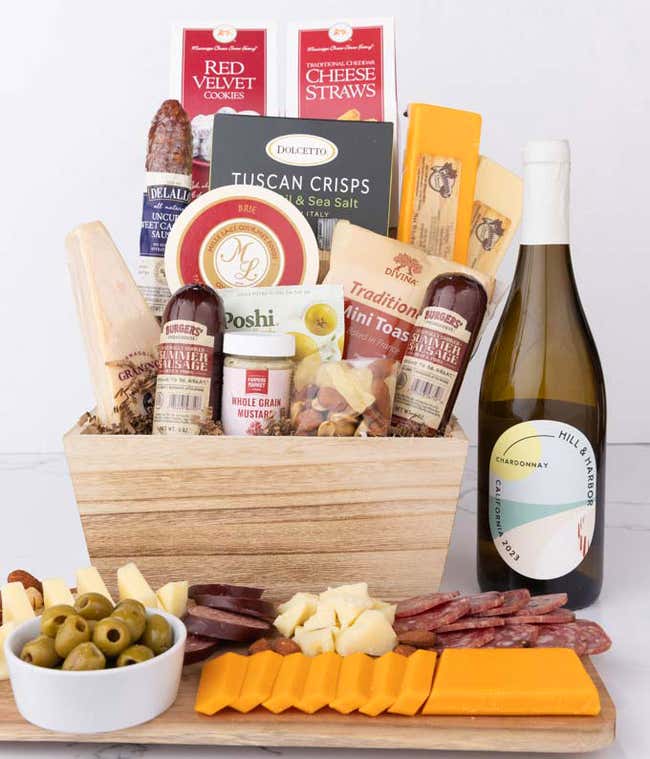 Wooden basket filled with 4 cheeses, 3 sausages, crackers, cookies, nuts, mustard, olives and crisps alongside a bottle of Hill &amp; Harbor Chardonnay.