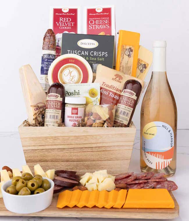 Wooden basket filled with 4 cheeses, 3 sausages, crackers, cookies, nuts, mustard, olives and crisps alongside a bottle of Hill &amp; Harbor Ros&eacute; wine.