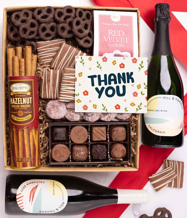 A gift box with chocolate pretzels, chocolate graham crackers, red velvet cookies, hazelnut wafer rolls, an 8 piece box of chocolates, 2 bottles of wine and a Thank You message card.