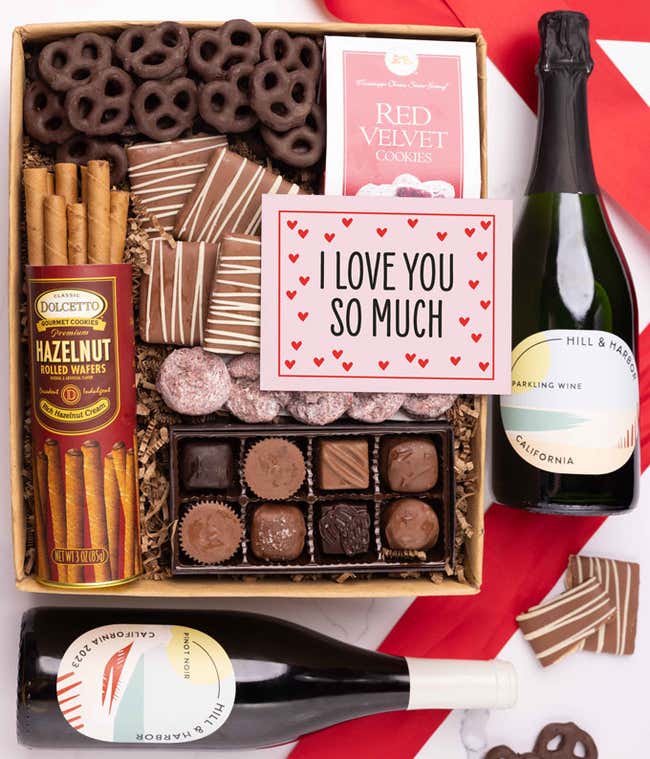 A gift box with chocolate pretzels, chocolate graham crackers, red velvet cookies, hazelnut wafer rolls, an 8 piece box of chocolates, 2 bottles of wine and an I Love You message card.