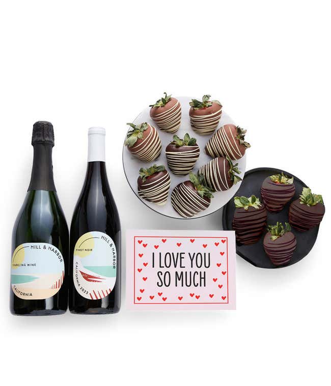 Two bottles of wine - Pinot Noir and Sparkling Wine are displayed beside 12 assorted chocolate-covered strawberries, drizzled in milk and dark chocolate and a card saying, 'I Love You'.