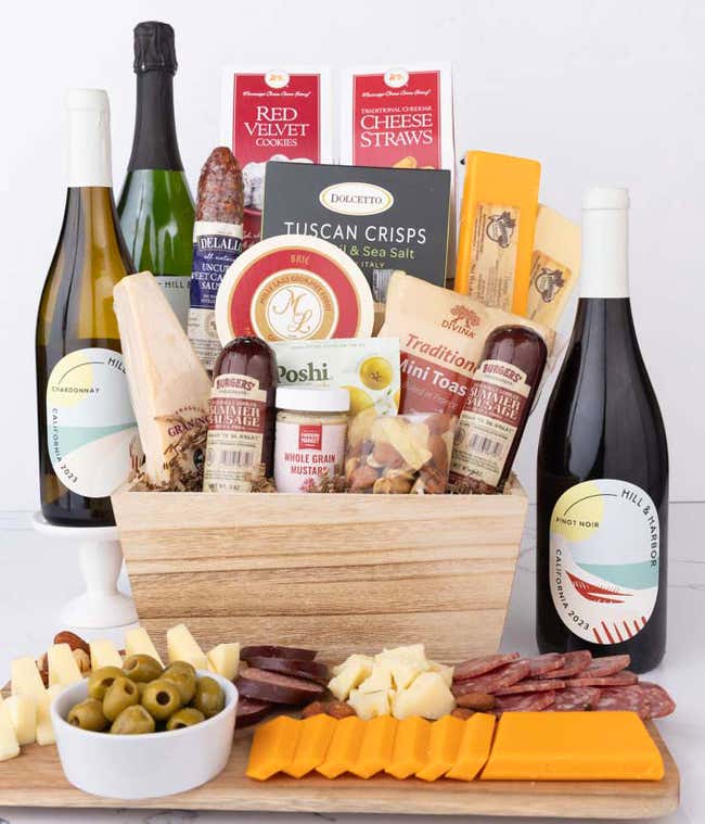 Wooden basket filled with 4 cheeses, 3 sausages, crackers, cookies, nuts, mustard, olives and crisps alongside 3 bottles of wine - Pinot Noir, Chardonnay &amp; Sparkling Wine.